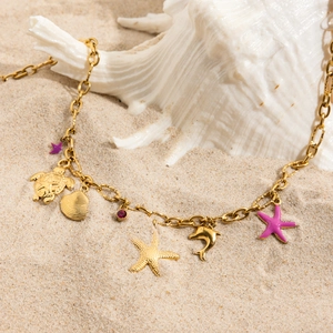Golden ocean theme necklace featuring starfish, shell, and turtle charms on a beach setup