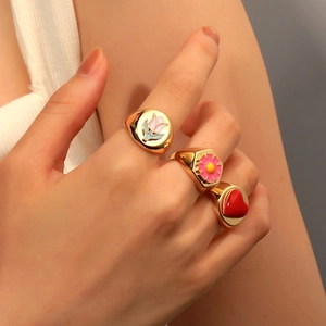 Detailed view of three gold rings with pink tulips, flowers and a red heart enamel design