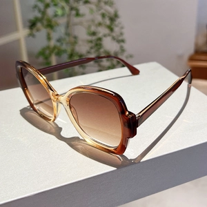 Detail of amber frame sunglasses with brown gradient lenses on a minimalist surface