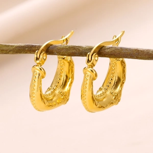 Detailed view of gold geometric U-shaped earrings with embossed pattern on a branch
