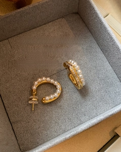 Macro shot of gold-tone C-shape earrings with pearls and zircons in a velvet box