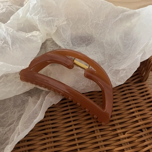 Brown amber hollow trapezoid hair claw clip placed inside a rustic woven basket