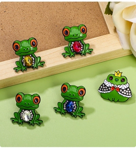 Detail of five cute frog brooches with colorful gemstones and enamel finish on cork background