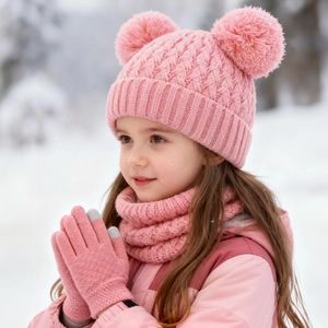 Close-up of pink cable-knit beanie with pom-poms, scarf, and gloves on a child in snow