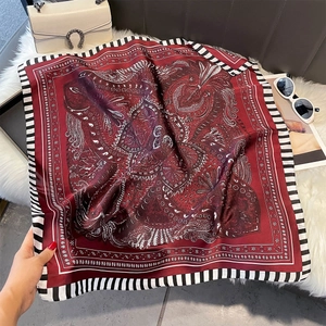 Detailed shot of burgundy paisley silk scarf on plush mat with elegant accessories