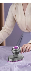 Detail of portable handheld garment steamer emitting steam on purple fabric texture