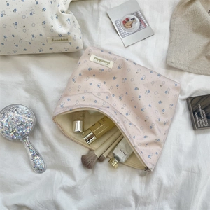 Flat lay of floral cotton makeup bags with skincare items on white fabric background