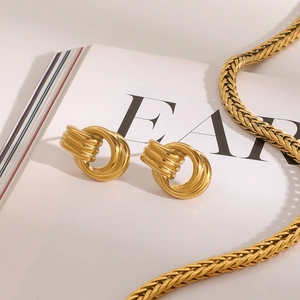 Detail shot of golden knotted geometric earrings and snake chain on an editorial book