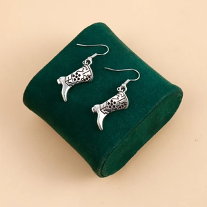 Détail des boucles d'oreilles bottes de cowboy argentées sur un support en velours vert