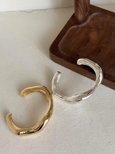 Detailed view of wide irregular polished gold and silver open bangles on textured base