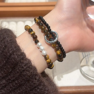 Detail of vintage tiger eye and pearl beaded bracelets set on a sweater sleeve