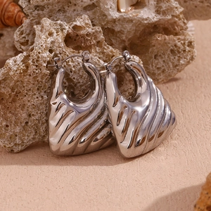 Detailed view of silver wave patterned hollow earrings on a natural textured rock background