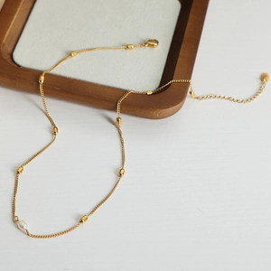 Elegant 18k gold plated titanium chain necklace with a single freshwater pearl on a wood tray