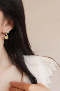 Close-up of golden bow earring with sparkling crystals and a yellow teardrop gemstone