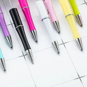 Colorful DIY beaded pens with plush pompoms and metal nibs on a grid paper background