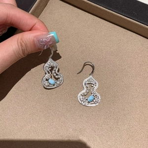 Detail of silver gourd earrings featuring blue gemstones and pearls on a beige tray