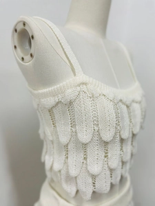 Detail of white knitted camisole with textured feather-like layered petal design on fabric