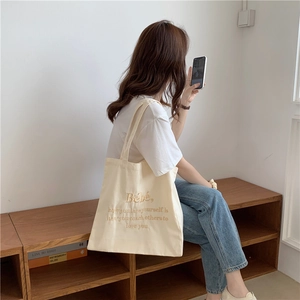 Detailaufnahme der cremefarbenen Canvas-Tasche mit brauner Bébé-Stickerei und Tragegriff