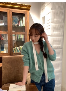Close-up of green knit cardigan V-neck with white tie-up strap and nice moment label