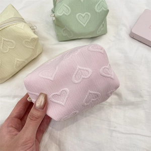 Détail de trousses à maquillage avec motifs de cœur en relief rose, menthe et jaune