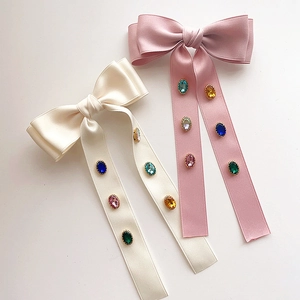 Detail of satin bow hair clips in beige and pink with colorful embedded crystals