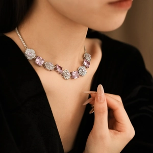 Close-up of a silver necklace featuring pink square stones and floral cubic zirconia charms