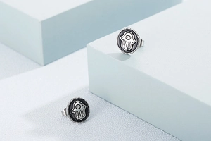 Detail view of round titanium steel earrings with black enamel palm and ghost motifs