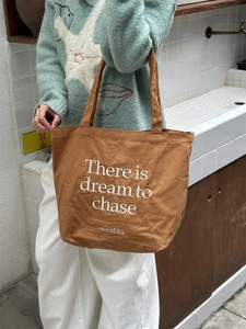Close-up of brown canvas tote bag featuring white dream to chase printed lettering
