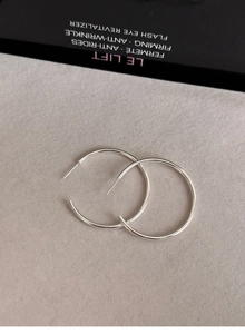 Detailed view of large silver hoop earrings on a textured gray background with minimalist style
