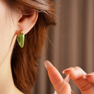 Close-up of vintage-style green enamel heart earring with gold trim on model ear
