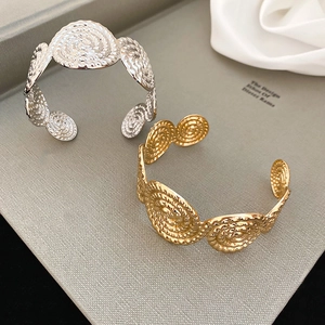 Close-up of gold and silver textured cuff bracelets with spiral woven metal design