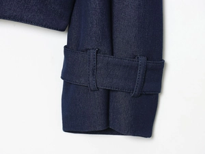 Detailed close-up of dark blue denim jacket cuff with strap and fine stitching