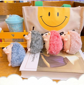 Detailed view of colorful plush hedgehog keychains arranged on a wooden desk with a canvas bag