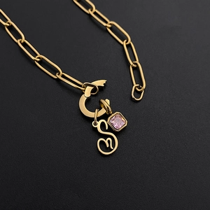 Close-up of gold paperclip chain necklace with cursive letter S and pink gem pendant