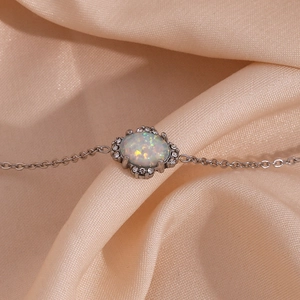 Details einer Silberkette mit ovalem Opalanhänger und Zirkon-Halo auf Champagner-Seide