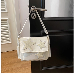 Detailed view of white canvas messenger bag with yellow plush star appliques hanging on a door