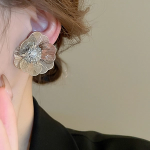 Close-up of a model wearing large hollow gold flower earrings with layered petals