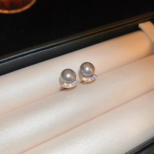 Macro shot of dark grey pearl earrings with sparkling diamond accents on a pink cushion