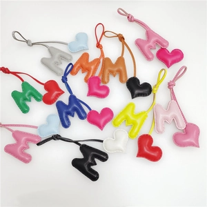 Detail showing various leather M-letter heart bag charms with contrast stitching