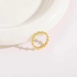 Detailed view of a 14K gold plated beaded ring leaning on a white ceramic plate