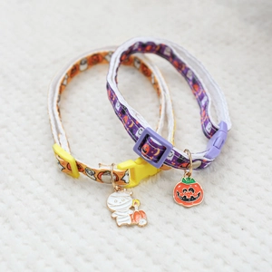 Detail of Halloween pet collars with pumpkin and mummy pendants on white textile