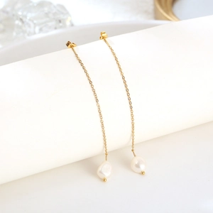 Minimalist gold chain tassel earrings featuring baroque pearls on a white luxury display