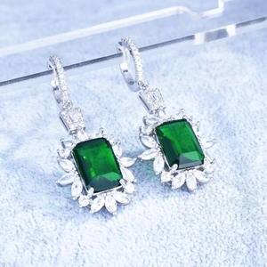 Detailed close-up of emerald-cut green crystal earrings with sparkling white halo setting