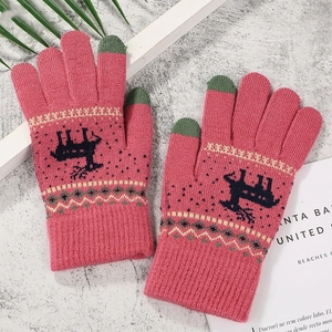 Detail of rose pink and green knit gloves with festive reindeer pattern on grey surface