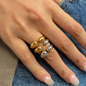 Close-up of teardrop-shaped open rings in gold and silver finish on a denim backdrop