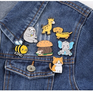 Detail of seven enamel animal pins like sloths and giraffes on a blue denim jacket pocket