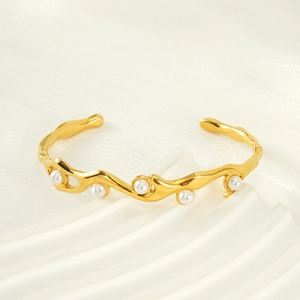 Elegant gold titanium steel wavy bangle with white pearls on a minimalist silk background