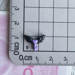 Macro shot of 1.5cm dark purple resin heart wing charm with ruler for size reference