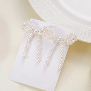 Detailed shot of bow-shaped pearl earrings on a branded white display card background
