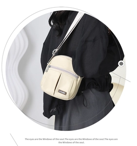 Detailed view of cream nylon crossbody bag with multi-zipper pockets worn by a model